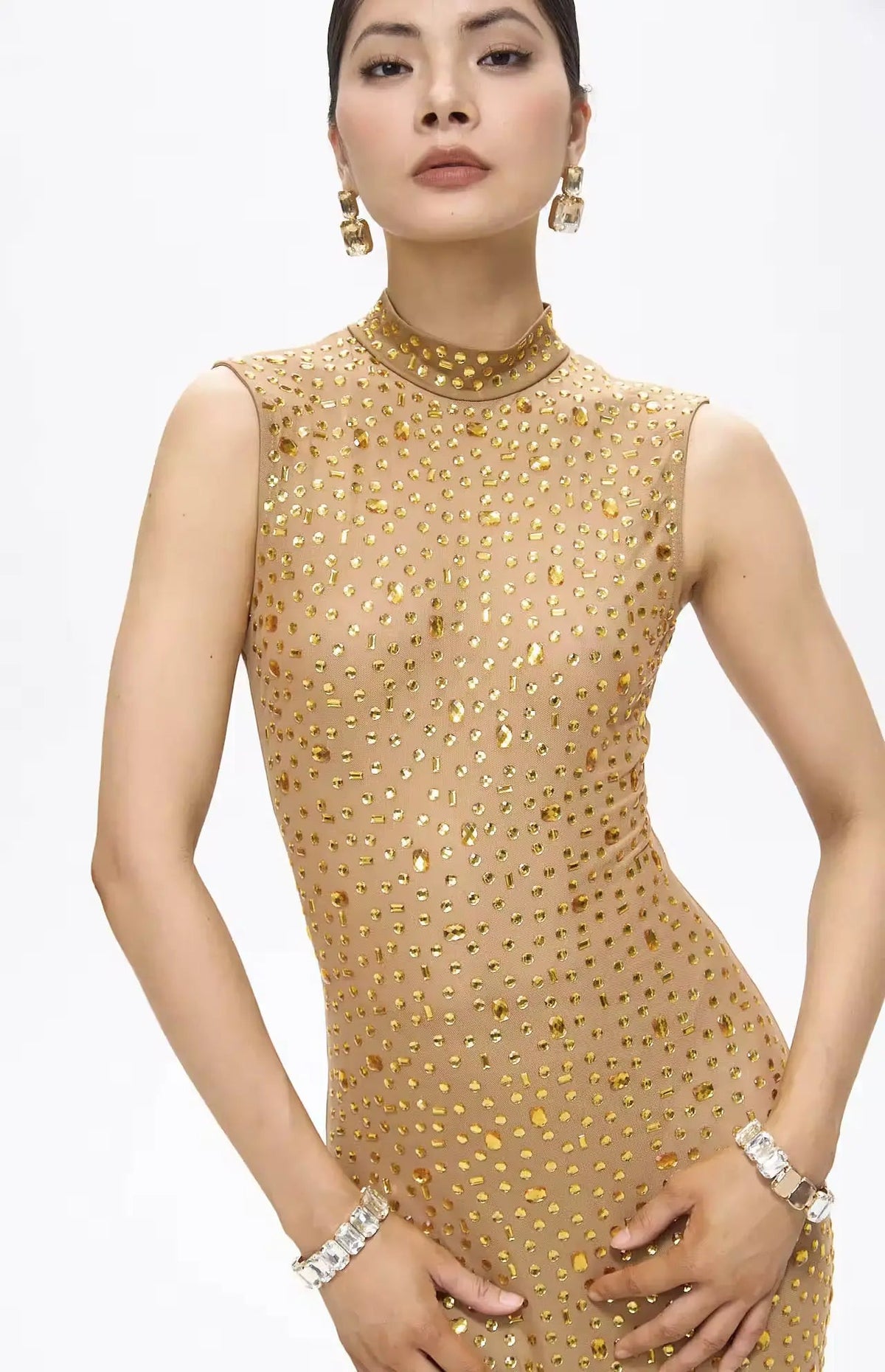 Woman wearing a gold beaded dress with jewelry on a white background